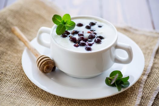 Cooked milk semolina porridge with berries and honey in a plate, on a wooden table.
