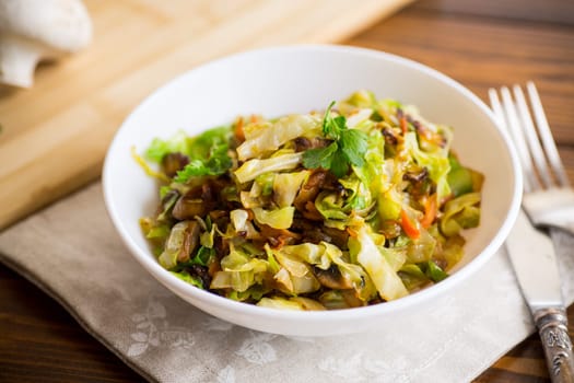 cabbage early fried with mushrooms, carrots and vegetables in a white bowl on a wooden table