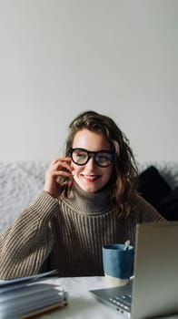 Young accountant manager working at home at the kitchen table, talking on the phone in front of the laptop, smiling, cute talking to CEO or bank support team about corporate account.