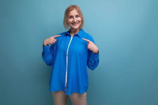 joyful smiling 50s middle aged woman in a blue shirt on a blue background with copy space.