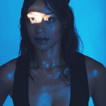 Spotlight, beauty and model in a neon studio posing for trendy beauty, cosmetics or skincare. Young, beautiful and woman from Mexico with a light reflection on her face isolated by a blue background