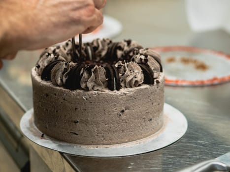 preparing brown frosted icing cup cake with cookies on top in the kitchen