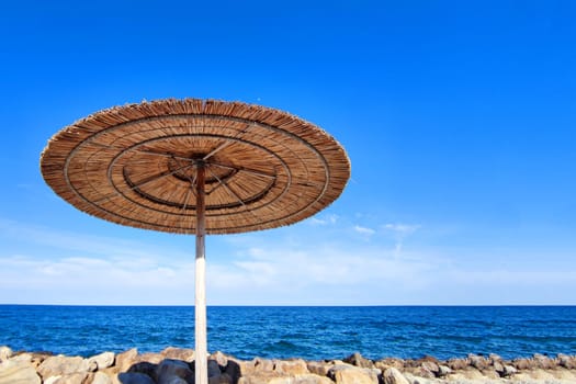 straw beach umbrella against the background of the sea horizon and a clear blue sky, copy space.