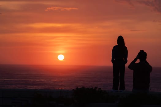 romantic lovers couple silhouettes. Beach photo shooting at sunset, man taking pictures of woman.