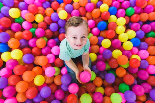 Happy child playing and having fun in kindergarten with colorful balls.
