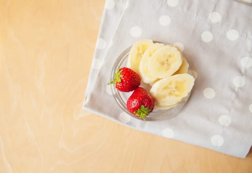 strawberry and banana on a glass plate on a wooden background