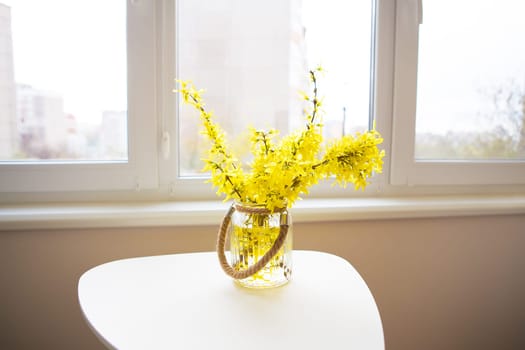 A bouquet of yellow flowers in a vase stand on a white table.
