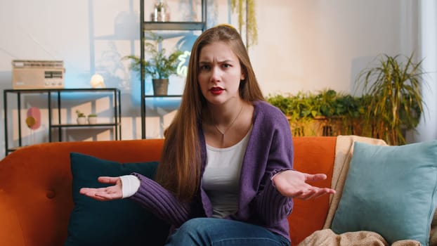 What. Why. Woman raising hands in indignant expression asking reason of failure demonstrating disbelief irritation by troubles at modern home apartment. Portrait of girl in living room sitting on sofa