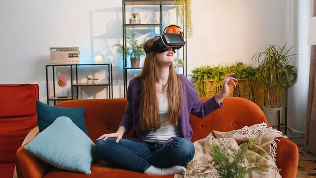 Portrait of woman using virtual reality futuristic technology VR app headset helmet to play simulation 3D 360 video game, watching film movie at modern home apartment. Girl in goggles sitting on couch