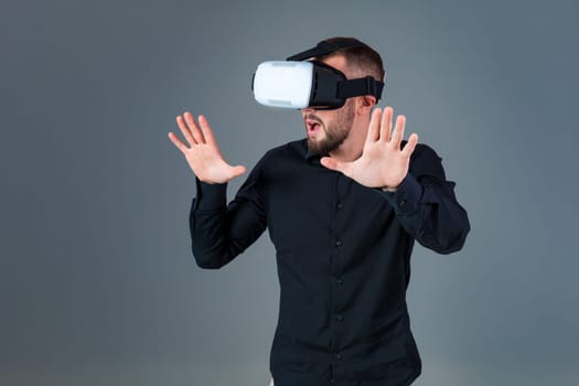 Emotional young man using a VR headset and experiencing virtual reality on grey background. A man dressed in a black shirt