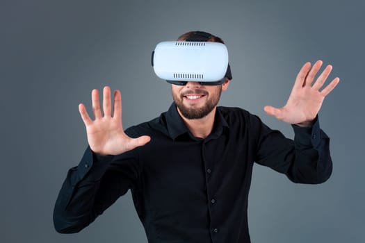Emotional young man using a VR headset and experiencing virtual reality on grey background. A man dressed in a black shirt