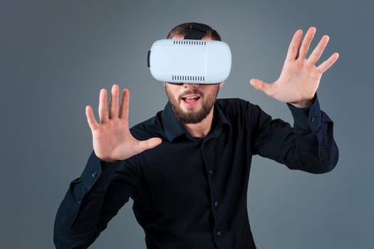 Emotional young man using a VR headset and experiencing virtual reality on grey background. A man dressed in a black shirt