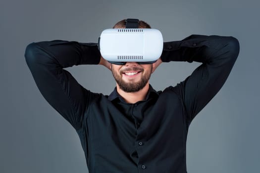 Emotional young man using a VR headset and experiencing virtual reality on grey background. A man dressed in a black shirt