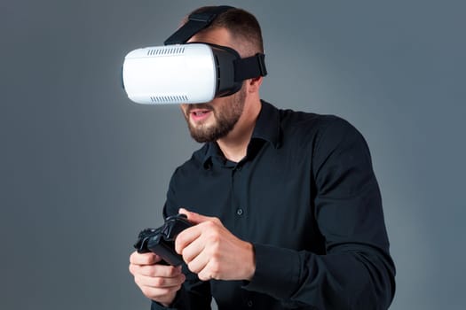 Emotional young man using a VR headset and experiencing virtual reality on grey background. A man dressed in a black shirt