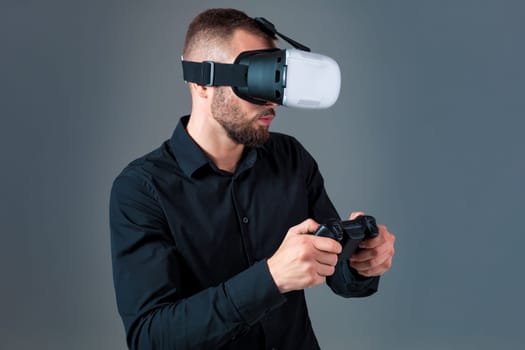 Emotional young man using a VR headset and experiencing virtual reality on grey background. A man dressed in a black shirt