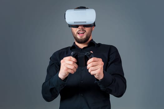 Emotional young man using a VR headset and experiencing virtual reality on grey background. A man dressed in a black shirt