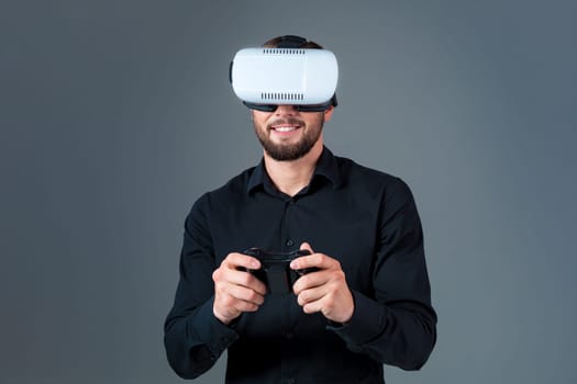 Emotional young man using a VR headset and experiencing virtual reality on grey background. A man dressed in a black shirt