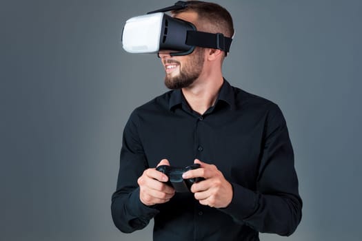 Emotional young man using a VR headset and experiencing virtual reality on grey background. A man dressed in a black shirt