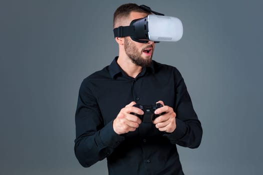 Emotional young man using a VR headset and experiencing virtual reality on grey background. A man dressed in a black shirt
