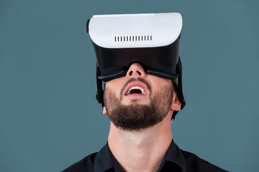 Excited young man using a VR headset glasses and experiencing virtual reality on grey blue background