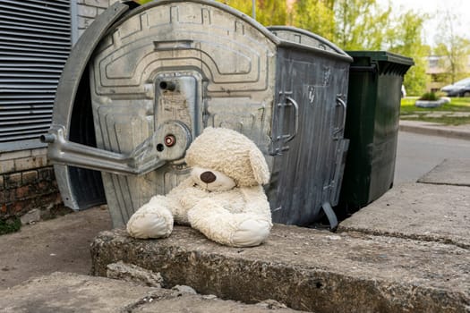 a sad abandoned teddy bear near the dumpsters. the concept of betrayal and abandonment. loneliness, pain and depression
