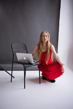 A business woman, lady blogger in a silk red dress is working, typing on a laptop apple . portrait blonde assistant of hands with computer MacBook, studio video production . Vertical