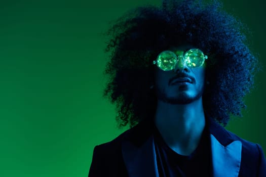 Fashion portrait of a man with curly hair on a green background with sunglasses, multinational, colored pink light, trendy, modern concept. High quality photo