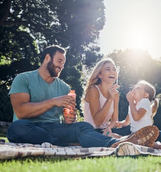 Family, happy and bubbles with picnic in park together for summer, relax and nature. Smile, spring and peace with parents playing with girl in countryside field for youth, lifestyle and happiness.