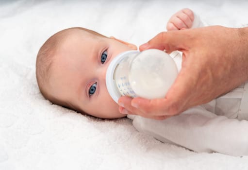 Beautiful baby eats formula from a bottle supported by his father.