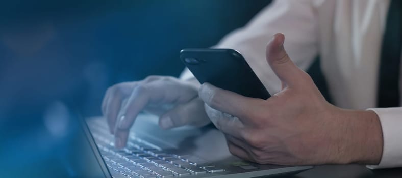 Close up of male hands with mobile phone and laptop keyboard.