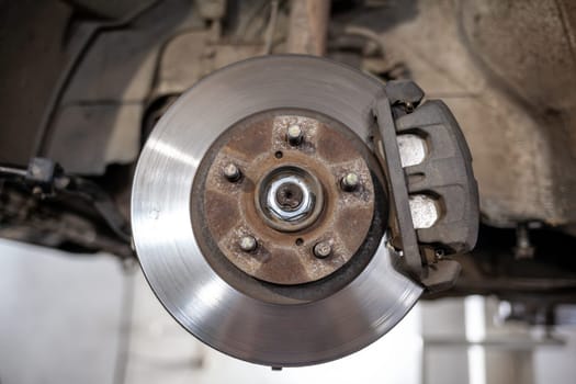 Disc brake of the vehicle for repair, in process of new tire replacement. Car brake repairing in garage.Suspension of car for maintenance brakes and shock absorber systems. Replacement of brake pads.