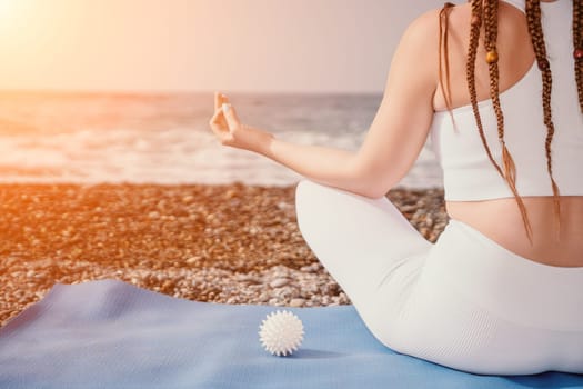 Woman yoga sea. Young woman with braids dreadlocks in white swimsuit and boho style braclets practicing outdoors on yoga mat by the ocean on sunny day. Women's yoga fitness routine. Healthy lifestyle, harmony