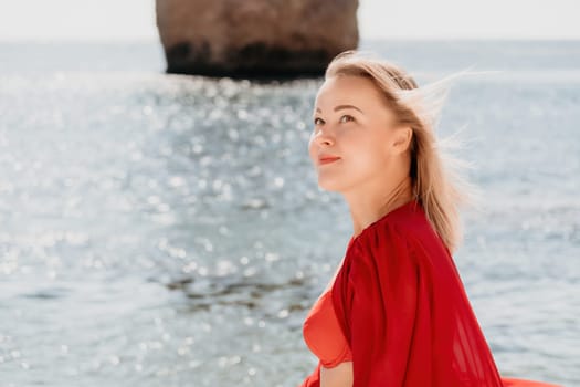 Woman travel sea. Young Happy woman in a long red dress posing on a beach near the sea on background of volcanic rocks, like in Iceland, sharing travel adventure journey