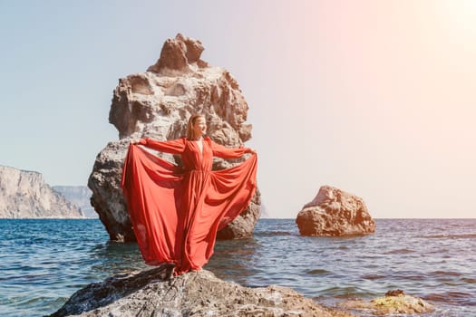 Woman travel sea. Young Happy woman in a long red dress posing on a beach near the sea on background of volcanic rocks, like in Iceland, sharing travel adventure journey