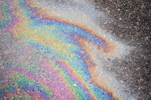 Oil stains from leaks in the car engine. Oil after rain makes spots with rainbow reflections refractive sun spectrum. Beautiful color mosaic, abstraction, ecology