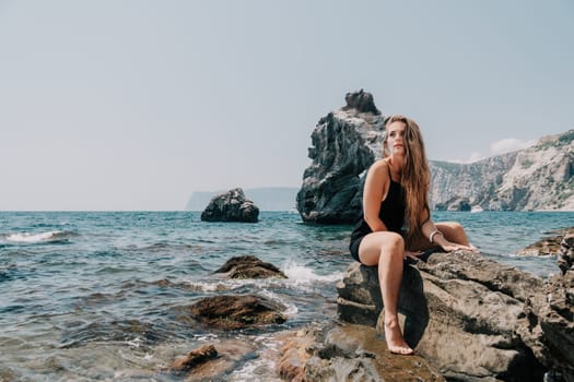 Woman travel sea. Young Happy woman in a long red dress posing on a beach near the sea on background of volcanic rocks, like in Iceland, sharing travel adventure journey