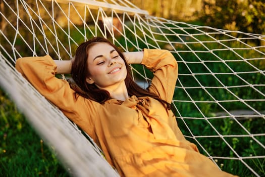 a happy woman is resting in a hammock with her eyes closed and her hands behind her head smiling happily enjoying the day. High quality photo