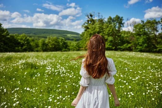 a red-haired woman in a light dress stands in a chamomile field with her back to the camera. High quality photo