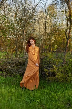 an elegant, sophisticated woman poses relaxed standing near a wicker fence at the dacha in a long orange dress. High quality photo