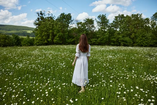 a red-haired woman in a light dress stands in a chamomile field with her back to the camera. High quality photo