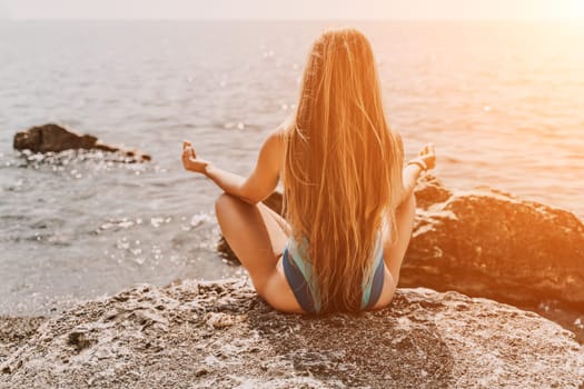 Yoga on the beach. A happy woman meditating in a yoga pose on the beach, surrounded by the ocean and rock mountains, promoting a healthy lifestyle outdoors in nature, and inspiring fitness concept