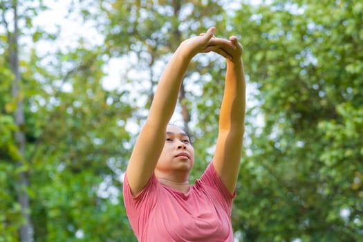 Young Asian woman in sportswear stretches before exercising in the park for a healthy lifestyle. Young healthy woman warming up outdoors. Healthy lifestyle concept.