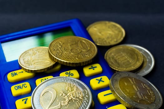 Money concept. Blue calculator with coins euro, close up, dark black background