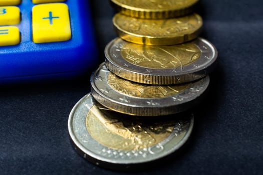 Money concept. Blue calculator with coins euro, close up, dark black background