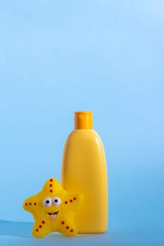 A yellow bottle with children's cosmetics with a place for a logo and funny toy on a light blue background. Copy space.
