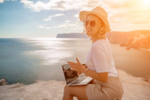 Freelance women sea working on the computer. Good looking middle aged woman typing on a laptop keyboard outdoors with a beautiful sea view. The concept of remote work