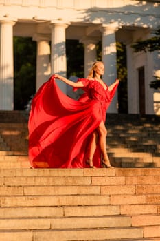 A woman in a long red dress against the backdrop of sunrise, bright golden light of the sun's rays. The concept of femininity, harmony