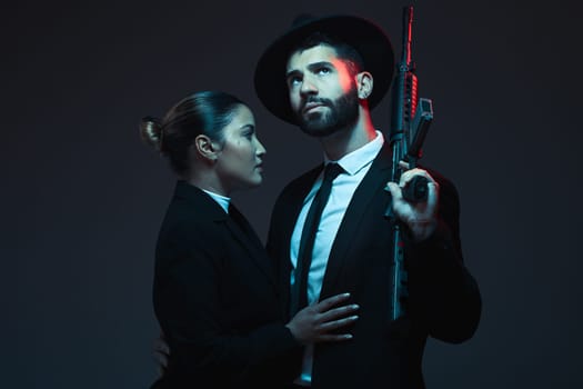Couple, fashion or weapon on dark studio background in secret spy, isolated mafia safety or crime lord security. Gangster love, woman or model with gun in stylish, trendy or fashion clothes aesthetic.