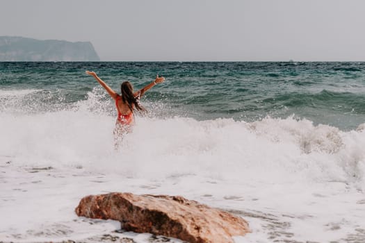 Woman travel sea. Young Happy woman in a long red dress posing on a beach near the sea on background of volcanic rocks, like in Iceland, sharing travel adventure journey