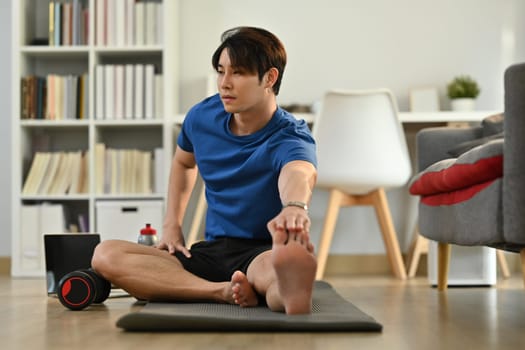 Active sportsman in fitness clothes stretching leg, preparing for morning workout at home. Healthy lifestyle concept.